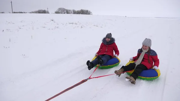 Glückliche Kinder rodeln im Winter im Schnee und winken mit den Händen. Kinder lachen und jubeln. Mädchen spielt in den Weihnachtsferien im Winterpark — Stockfoto