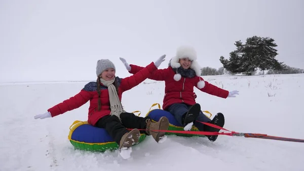 孩子们在雪中滑行在一个充气的雪管和波的手。快乐的女孩骑着雪橇在雪地上滑行。孩子们在公园里玩圣诞节假期在冬天 — 图库照片