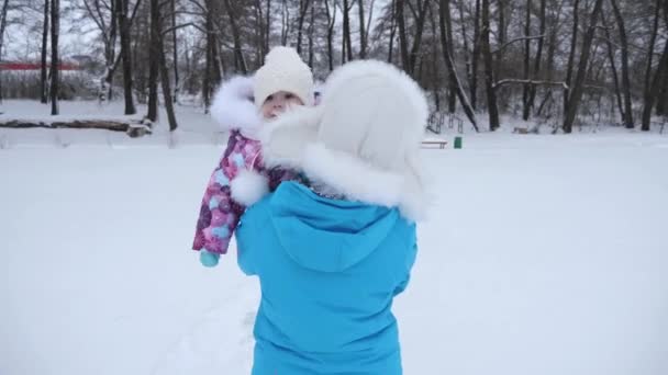 Мама носить на руках маленьку дитину, що йде по засніженій дорозі взимку. Дочка сміється з мами. Батько гуляє з дитиною в парку. Зима — стокове відео