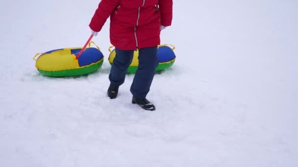 Adolescente sube a la montaña nevada de invierno sosteniendo platillo de nieve. Juegos de invierno al aire libre. Navidad — Vídeo de stock