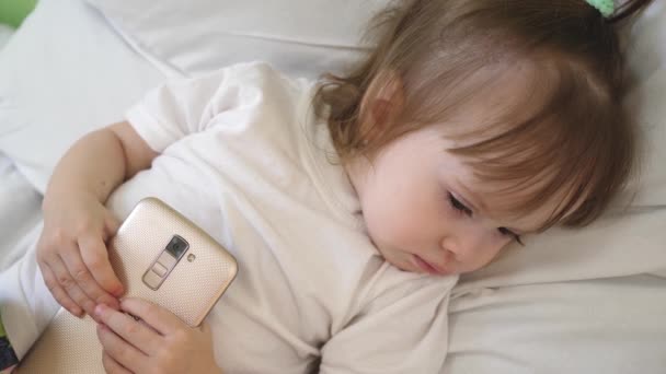 Μικρό μωρό ξαπλωμένη στο νοσοκομείο στο κρεβάτι και αποκοιμιέται με το τηλέφωνο στο χέρι — Αρχείο Βίντεο