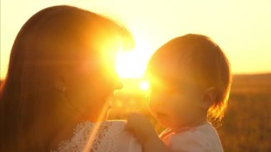 Anne küçük kızı onun kollarında tutar. mutlu aile parkta sıcak yaz akşam gün batımını izlemek