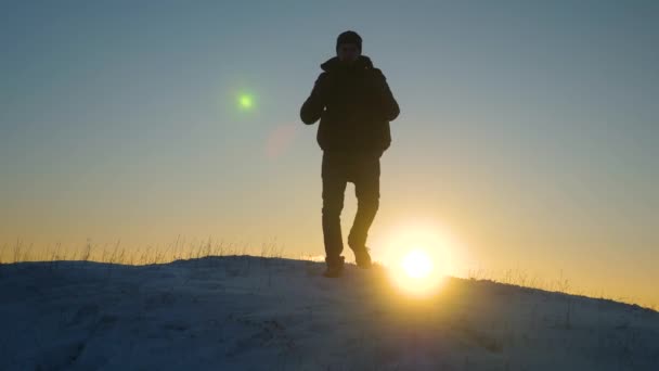 バックパックを持つ旅行者は、青空夕日の光線で雪に覆われた丘から降りる。日当たりの良い明るいの光線で雪冬に歩く観光客のシルエット — ストック動画