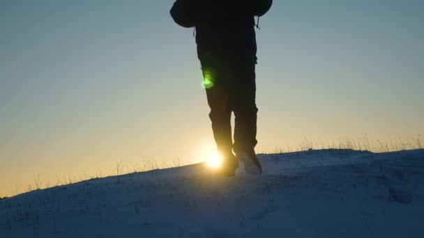 Manliga turister med ryggsäckar klättra till toppen på bakgrund av vackra himmel och sol. resenär med ryggsäck går på snöiga kulle i solnedgången mot den blå himlen strålar. — Stockvideo