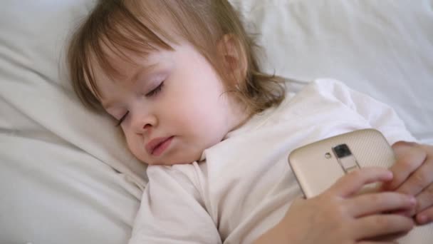 Bambino è sdraiato sul cuscino e in possesso di una compressa. Carino bambino che dorme a letto con smartphone . — Video Stock