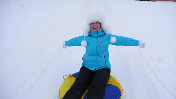 Bela jovem desliza na neve em um tubo de neve inflável e mão de ondas. Menina feliz desliza através da neve no trenó. menina jogando no parque para as férias de Natal no inverno — Fotografia de Stock