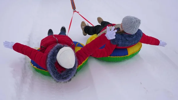 Crianças em jaquetas vermelhas passeio através da neve no inverno em um tubo de neve inflável e jogar super-heróis. meninas felizes relaxando no parque de inverno para férias de Natal. Movimento lento — Fotografia de Stock