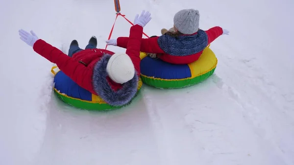 I bambini in giacche rosse cavalcano attraverso la neve in inverno su un tubo da neve gonfiabile e giocano super eroi. ragazze felici rilassarsi nel parco invernale per le vacanze di Natale. Rallentatore — Foto Stock