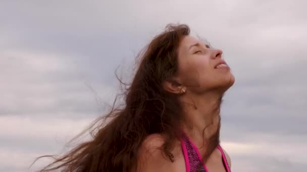 Hermosa chica con el pelo largo desaliñado por el viento se regocija en la lluvia y sonrisas. La mujer camina con el tiempo nublado por la noche. Primer plano — Vídeos de Stock