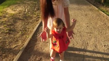 Anne küçük bebek yürüme ve Park yol boyunca yürüyüş gülümseyen öğrenir yakalar. Ağır çekim