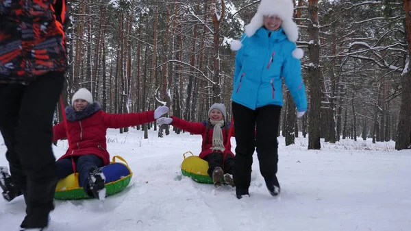 Glückliche Väter und Mütter ziehen mit Kindern Schlitten im Winterwald. Eltern spielen im Winter mit Kindern in einem verschneiten Park. glückliches Familienrodeln während der Weihnachtsfeiertage. — Stockfoto