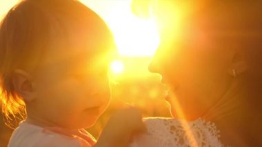 Küçük kız anne ile oynuyor. Günbatımı altın güneş, anneler kollarında oynarken mutlu küçük bebek.