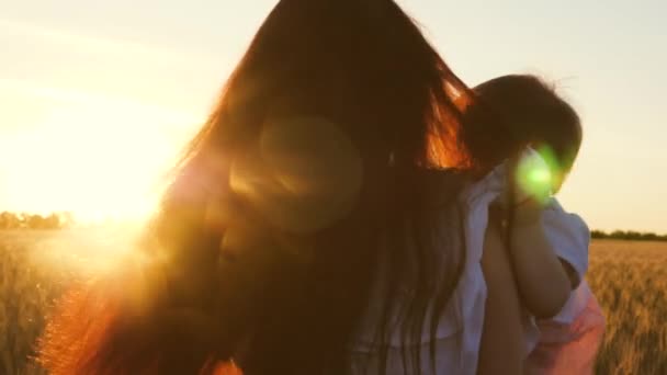 Die junge Mutter mit ihrer kleinen Tochter tanzt und lacht im Weizenfeld, im Strahlen eines wunderschönen Sonnenuntergangs. Zeitlupe. Nahaufnahme — Stockvideo