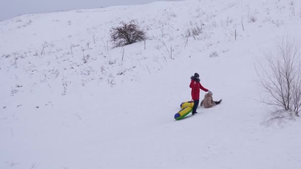 Nastoletnie dziewczyny jeździć od wysokiej góry śnieżne zimą na śniegu spodek. Dzieci gry zimą na świeżym powietrzu. Szczęśliwe dziecko na święta Bożego Narodzenia — Wideo stockowe