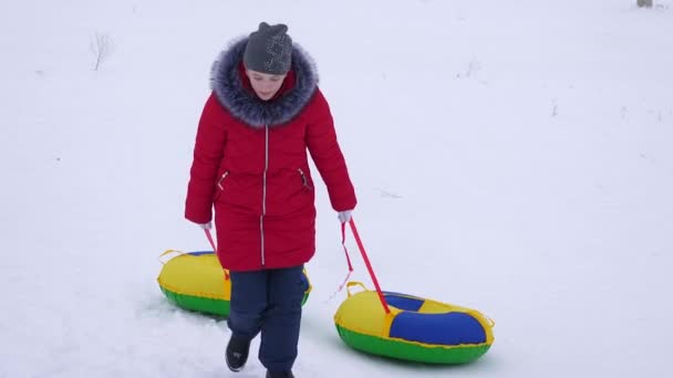 Adolescente menina sobe alta montanha nevada segurando dois discos de neve. Férias de Natal — Vídeo de Stock