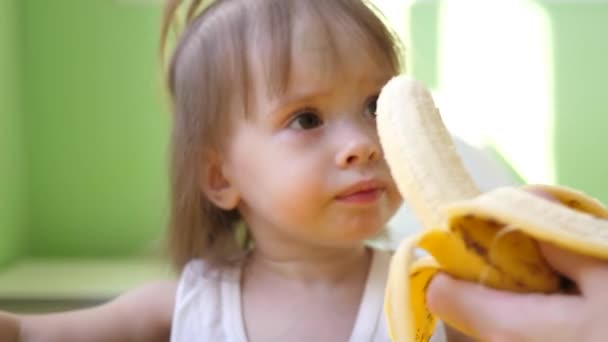 Mom feeds little baby banana sitting at table in kitchen. Complement for small children. Sweet snack kid — Stock Video