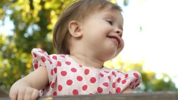Маленький счастливый ребенок улыбается, играя в парке на скамейке — стоковое видео