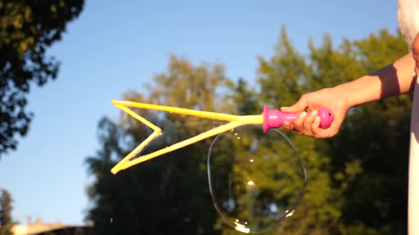 Mädchen bläst große Blasen im Stadtpark vor blauem Himmel. Nahaufnahme. Zeitlupe — Stockvideo