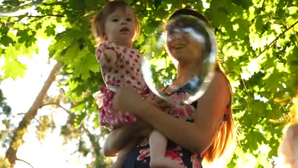 姉は、妹を果たしています。子供たちは、都市公園における大きくて透明な石鹸の泡をキャッチします。幸せな子供時代の概念. — ストック動画
