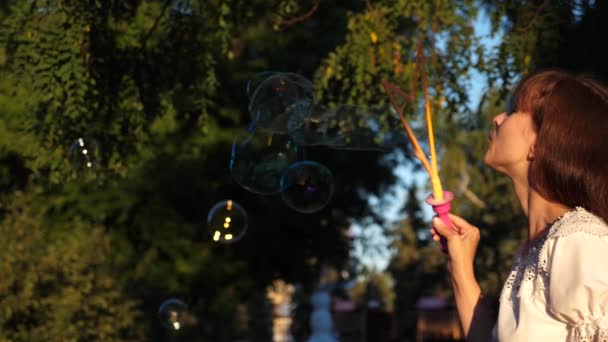 Menina deixa grandes bolhas no parque da cidade e sorrindo. Movimento lento — Vídeo de Stock