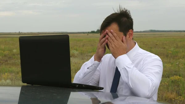 Hombre de negocios en camisa azul y blanca está trabajando en el campo en el ordenador en el techo del coche . — Foto de Stock