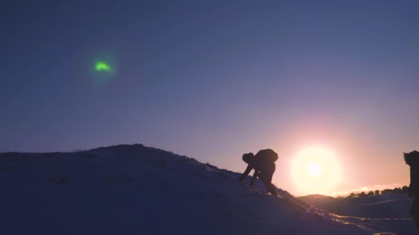 バックパックで観光客は太陽の明るい光線の丘の頂上に互いを助けます。雪の山に登山は彼らの成功を喜ぶ、手を上げるし、喜んでジャンプします。スポーツ観光コンセプト — ストック動画