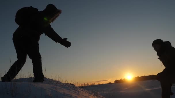 Альпинисты помогают другу подняться протянув руку помощи. два туриста на вершине горы. Силуэт путешественников зимой на холме в ярких лучах солнца. концепция спортивного туризма — стоковое видео