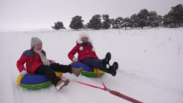 Adolescentes montam estrada nevada no disco de neve e riem. As crianças brincam no inverno com trenós. Movimento lento — Vídeo de Stock