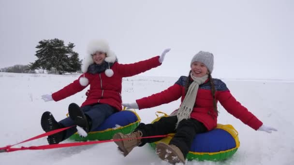 Nastoletnich dziewcząt lecą w locie na zaśnieżonej drodze snowy płycie i śmiać się. Dzieci bawią się w zimie na sanki. — Wideo stockowe