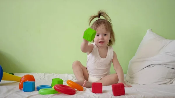 Niño juega con cubos multicolores en una cama blanca y se los lanza a su madre. Juguetes educativos para niños de preescolar y jardín de infantes. Juguete para niño . —  Fotos de Stock