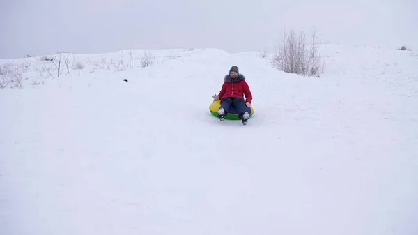 Fröhliches junges Mädchen gleitet von einer hohen Schneerutsche auf eine aufblasbare Schneeröhre. Kinder spielen im Winter im Park in den Weihnachtsferien. rollt im Schlitten bergab. — Stockfoto