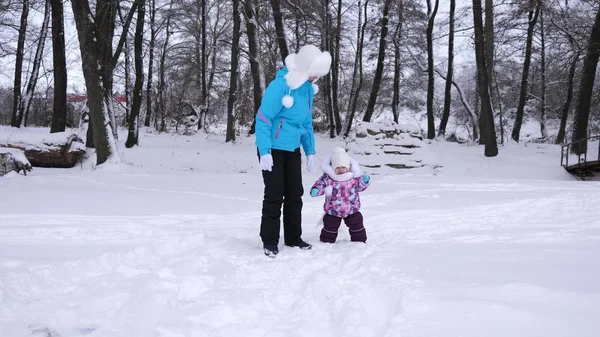 Mama prowadzi ręka jej córeczkę podczas spaceru przez park pokryte śniegiem zimą. Matka spacery z dzieckiem, który jest niegrzeczny i płacz. Boże Narodzenie — Zdjęcie stockowe