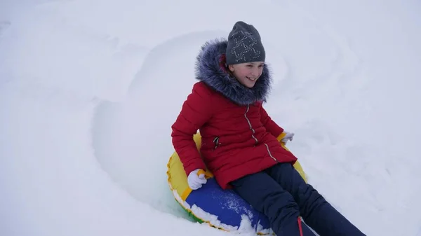 Teen girl gioca in un parco invernale durante le vacanze di Natale. scivoli ragazza in inverno nella neve da alta collina su slitta e un tubo di neve gonfiabile. Rallentatore . — Foto Stock