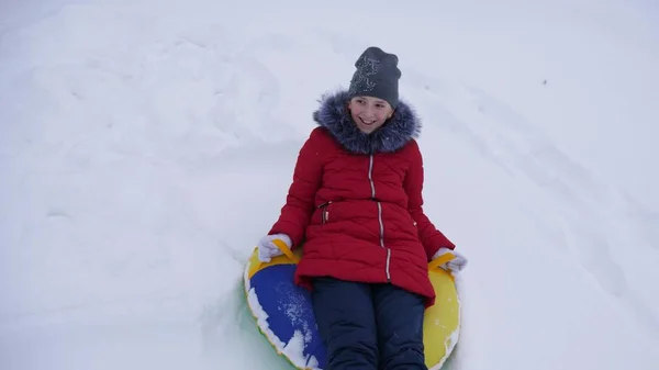 Teenie-Mädchen spielt an den Weihnachtsfeiertagen in einem Winterpark. Mädchen rutscht im Winter im Schnee von einem hohen Hügel auf Schlitten und einem aufblasbaren Schneeröhrchen. Zeitlupe. — Stockfoto