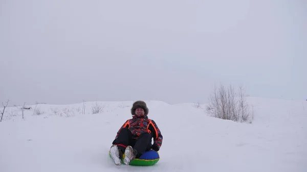 O homem feliz desliza da corrediça alta da neve um tubo inflável da neve. pessoa jogar no inverno no parque nas férias de Natal. rola colina abaixo em trenó . — Fotografia de Stock