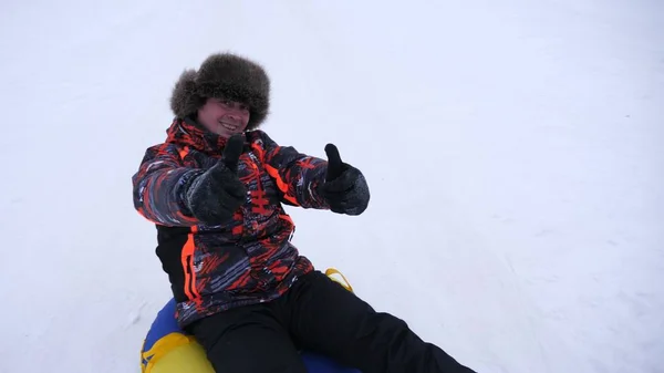 Hombre se desliza deslizarse en la nieve en un tubo de nieve inflable y olas mano. Los hombres felices se deslizan a través de la nieve en trineo. hombres jugando en el parque para las vacaciones de Navidad en invierno —  Fotos de Stock