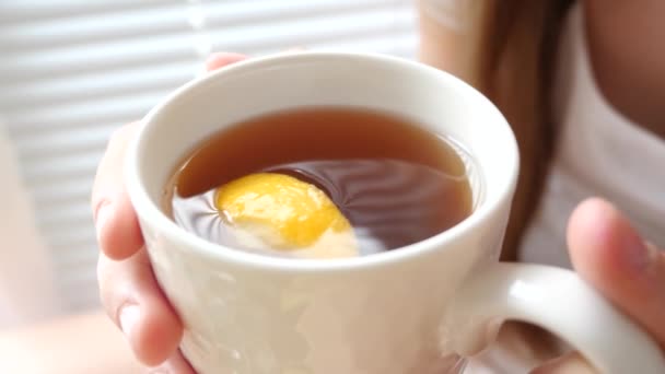 Thé d'or chaud avec tranche de citron est bu par la fille qui est debout par la fenêtre . — Video