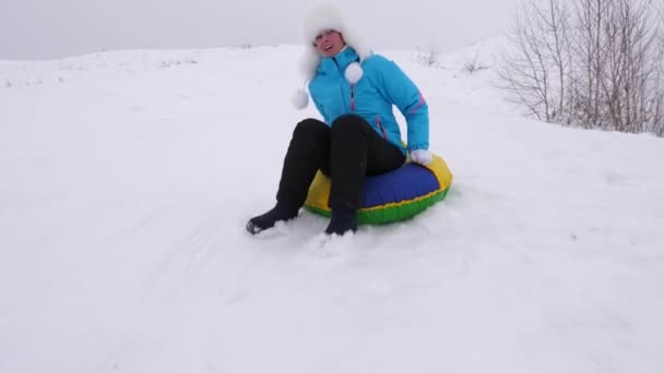 Девушка едет с высокой горы на снежной тарелке по снегу зимой и смеется с удовольствием. Веселая женщина катается на санках. Рождество — стоковое видео
