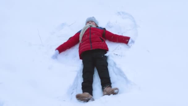 Chica muestra ángel de la nieve en la nieve blanca en invierno. El niño está jugando con nieve. Vacaciones de Navidad — Vídeos de Stock