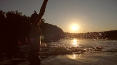 Genç kız nehirde gün batımında banyoları ve su sıçramalarına elleriyle yavaş çekim
