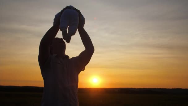 Papa circuitnadering baby rond zijn armen bij zonsondergang. Slow motion. — Stockvideo