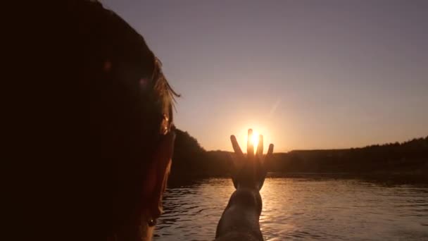 Jong meisje legt haar hand naar zon op de achtergrond van de rivier — Stockvideo