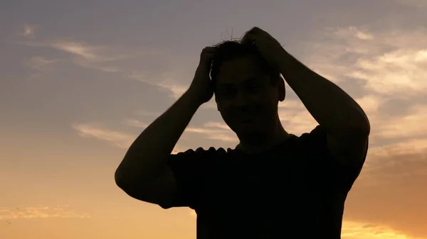silhouette of man is scratching his head against sky
