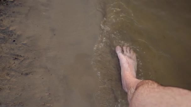 Mens voeten lopen blootsvoets langs de kust, opspattend waterdruppels in verschillende richtingen. Slow-motion. Close-up. — Stockvideo