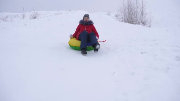 Meisje rijdt sneeuw schotel van hoge besneeuwde berg en lacht. Kind rodelen in de winter — Stockvideo