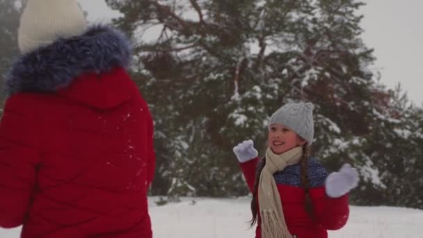 Gelukkige jonge geitjes spelen sneeuwballen in het dennenbos en lachen. Vrolijke tiener meisjes spelen met sneeuw in de winter in pine park. Kerst — Stockvideo