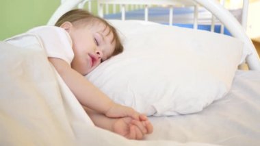 Küçük bebek hastane koğuşunda beyaz yatak örtüsü üzerinde uyku. Hastane ortamında çocukların tedavisinde. Hasta çocuk sağlığı hastanede geliştirir