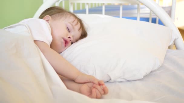 Малыш спит в палате больницы на белом одеянии. Лечение детей в условиях стационара. Больной ребенок улучшает свое здоровье в больнице — стоковое видео