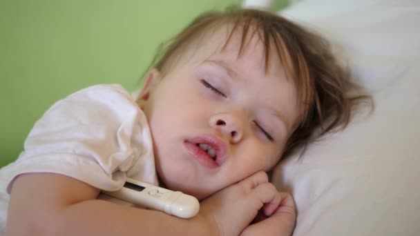 La température de l'enfant est mesurée avec un thermomètre dans la salle d'hôpital. Gros plan. Bébé dort à l'hôpital sur un lit blanc . — Video