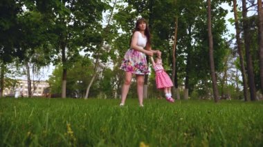 Genç Anne küçük kızı çevresinde ve gülüyor döner. Mutlu anne ve birlikte parkta eğleniyor ve gülen çocuk. Şehir çocuğunun dadı yürür